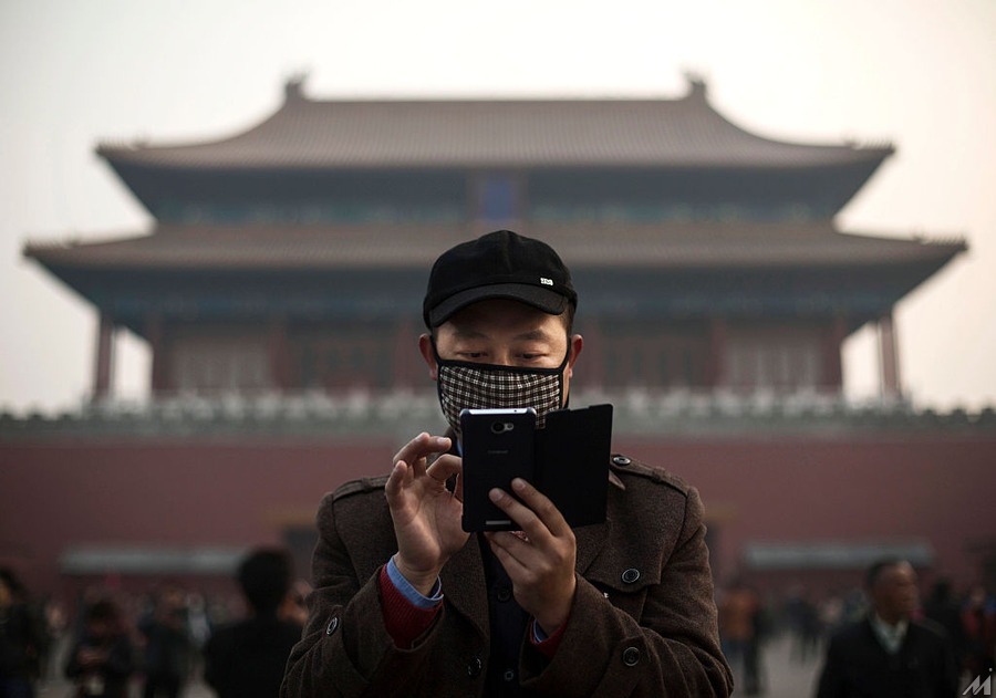 <p>BEIJING, CHINA – NOVEMBER 20:  A Chinese man wears a mask to protect against pollution as he uses his smartphone on a hazy day outside the Forbidden City November 20, 2014 in Beijing, China. United States President Barack Obama and China’s president Xi Jinping agreed on a plan to limit carbon emissions by their countries which are the world’s two biggest polluters at a summit in Beijing last week.  (Photo by Kevin Frayer/Getty Images)</p>